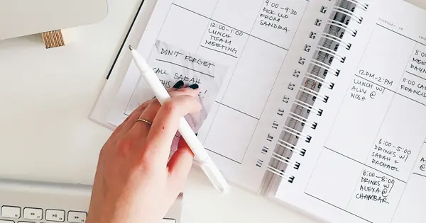 يد تكتب خطة الأسبوع في دفتر مواعيد بجانب لوحة مفاتيح